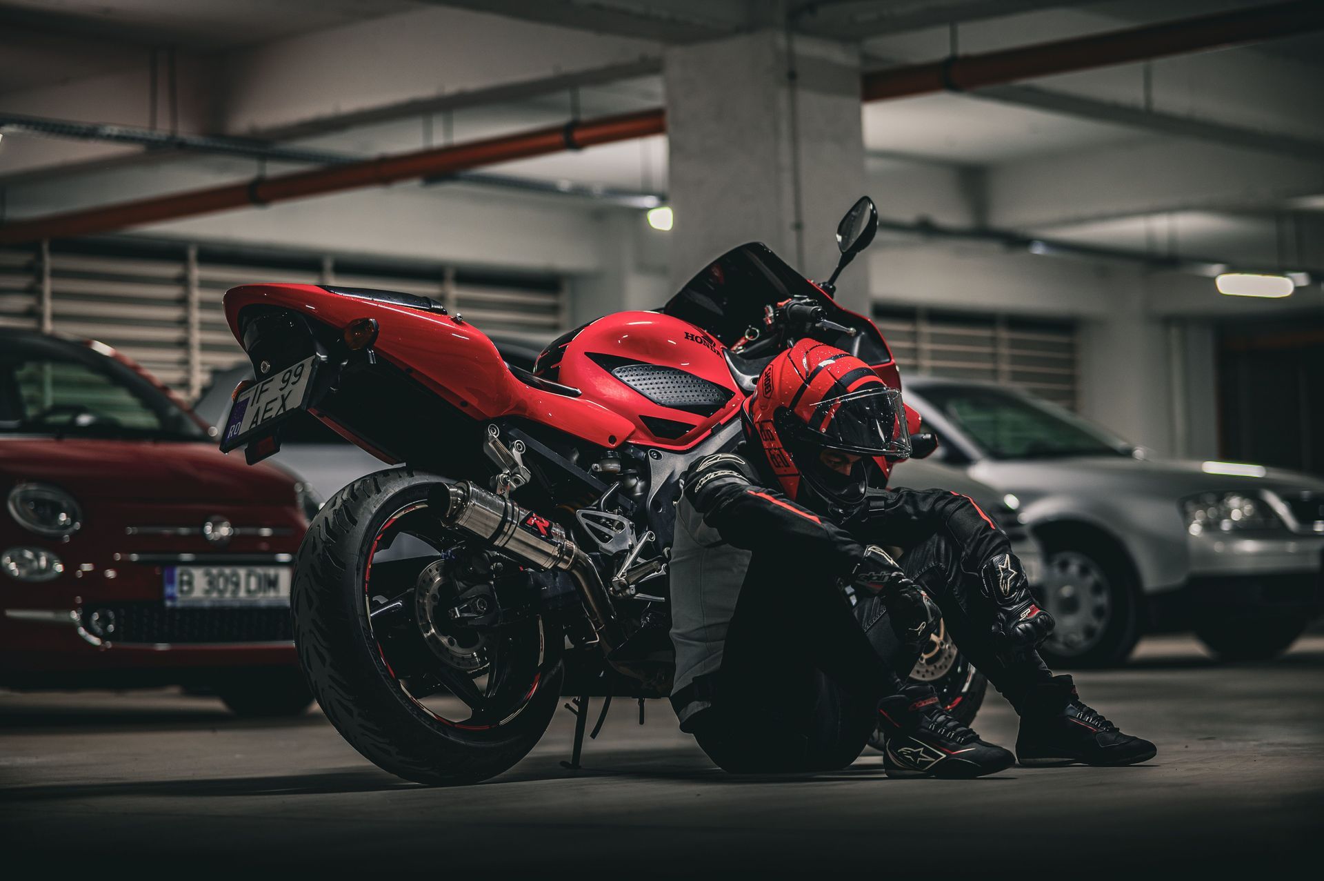 Red sport motorcycle parked in a dim garage beside cars, with a person crouched next to it.
