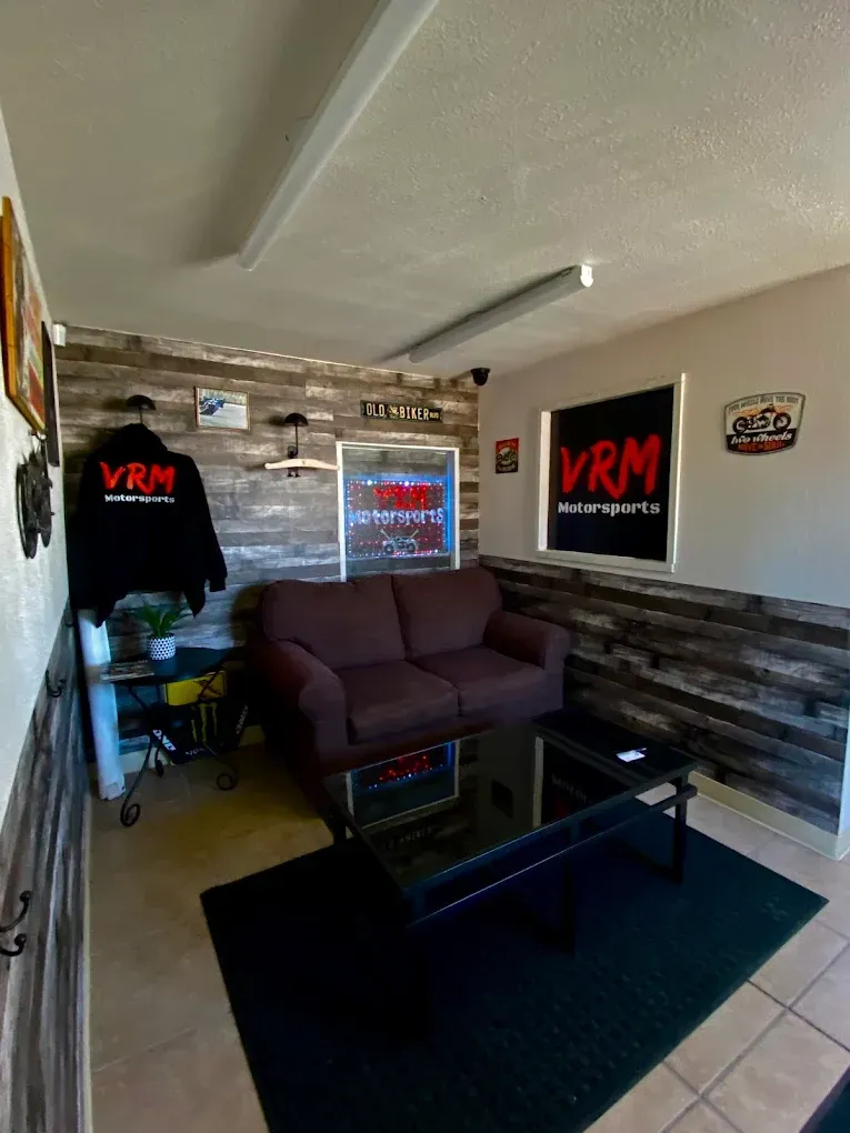 Small lounge with dark purple couch, glass coffee table, black rug, and VRM banners on the walls.
