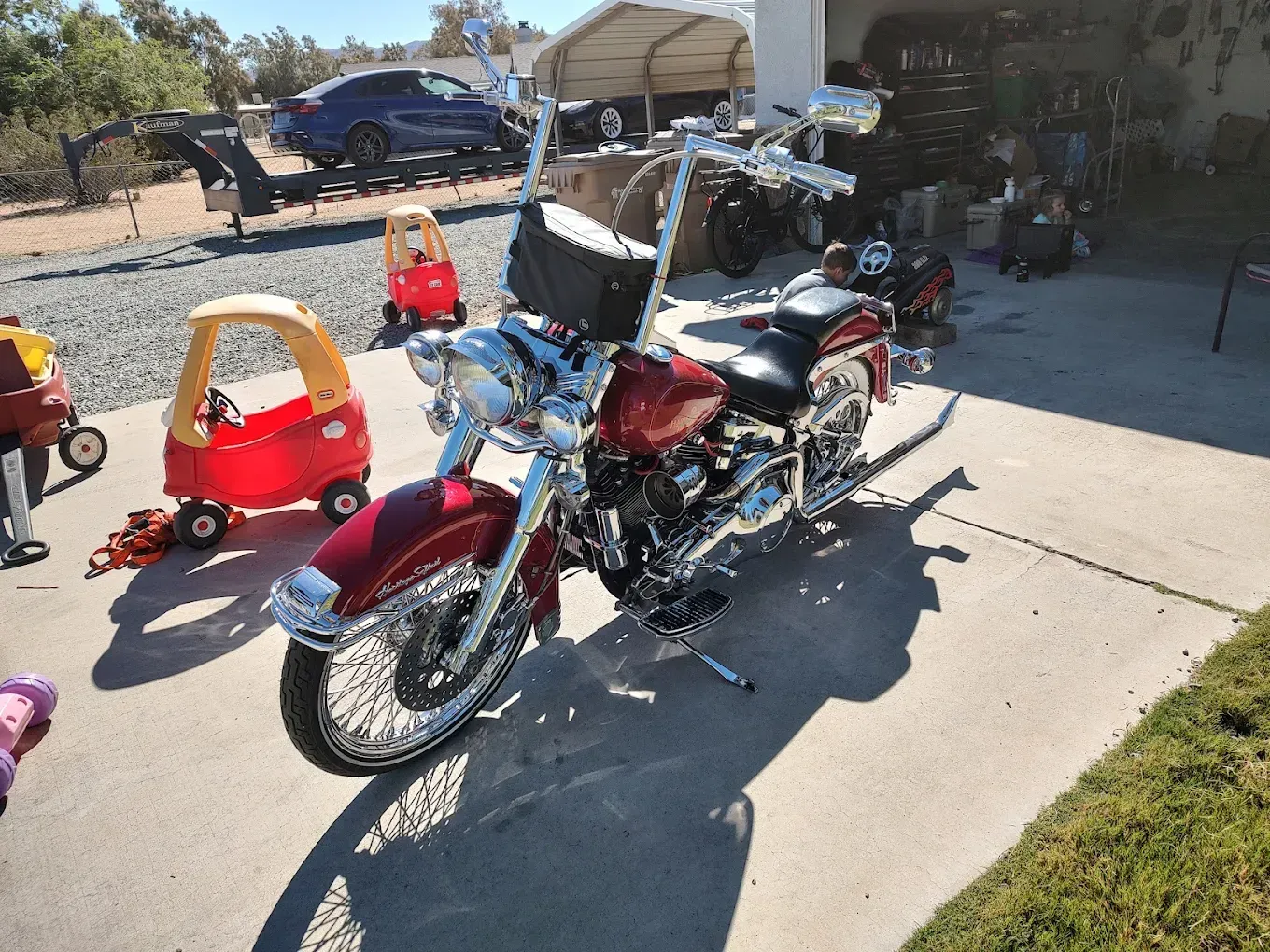 Red and chrome motorcycle parked in a driveway beside a red toy car and garage clutter.