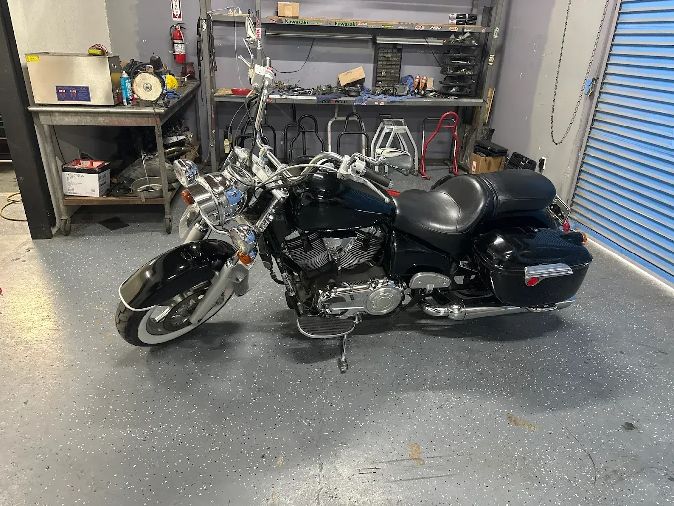 Black touring motorcycle parked in a garage, with tools and shelves in the background.
