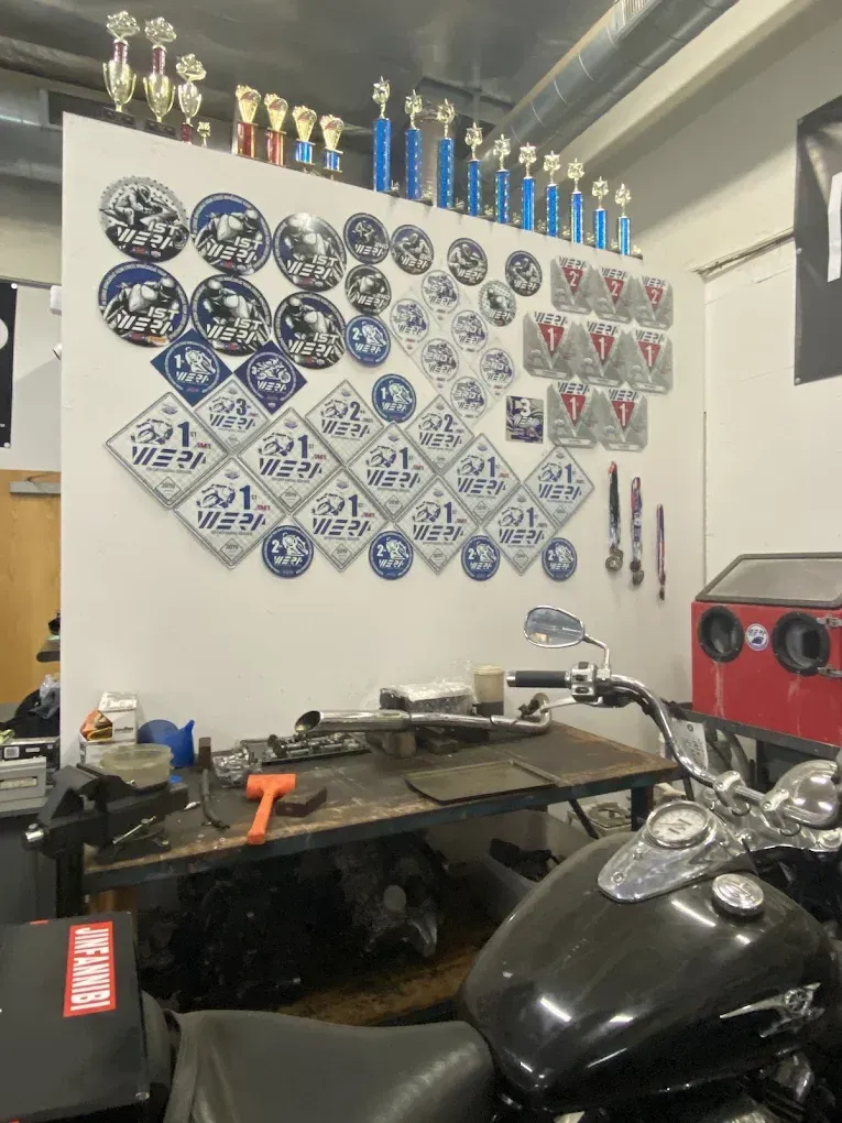 Garage wall with rows of blue and white plaques, trophies on a shelf, and a black motorcycle in front.
