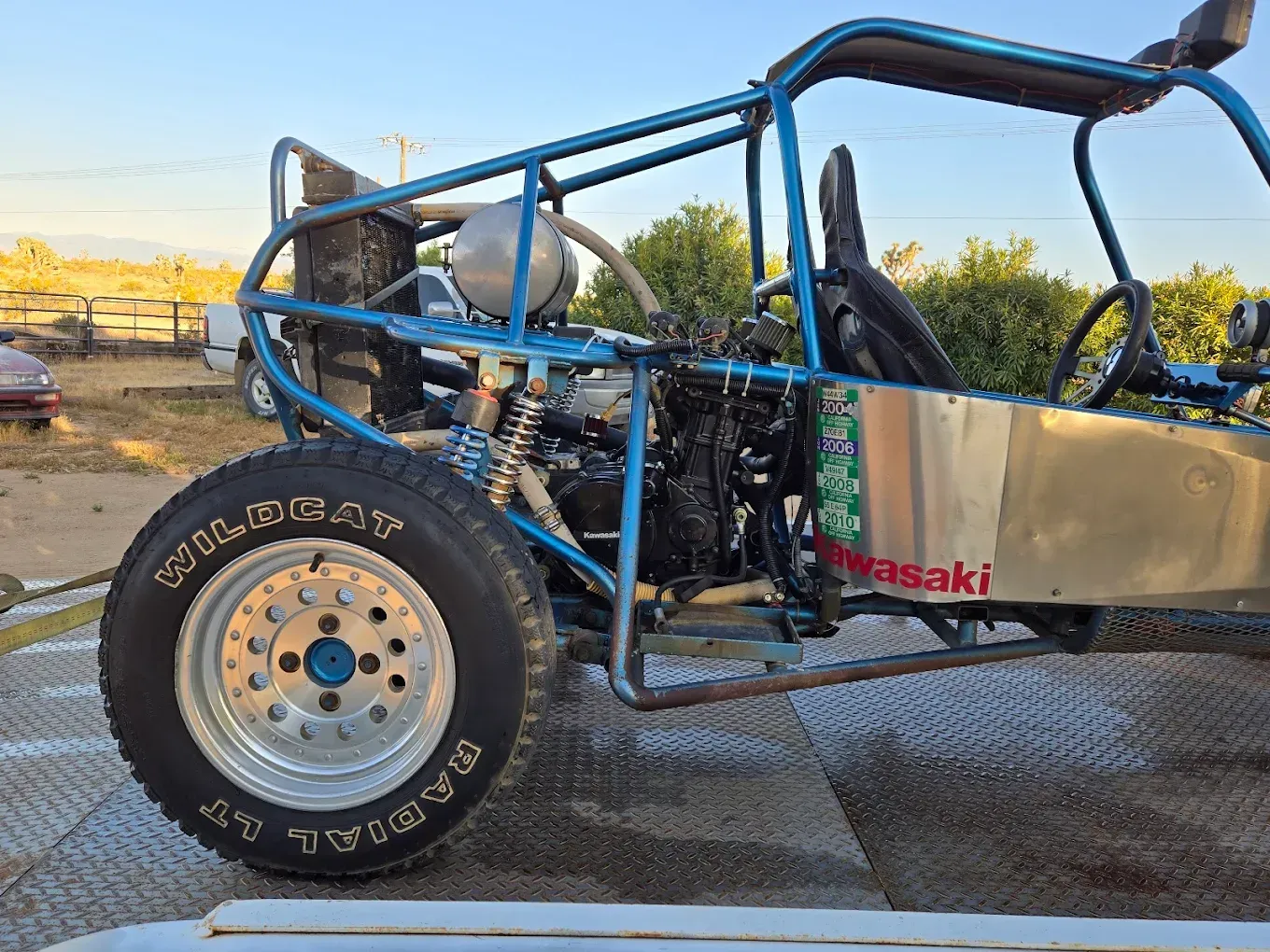 Blue tube-frame off-road buggy with large tires parked on a trailer at sunset