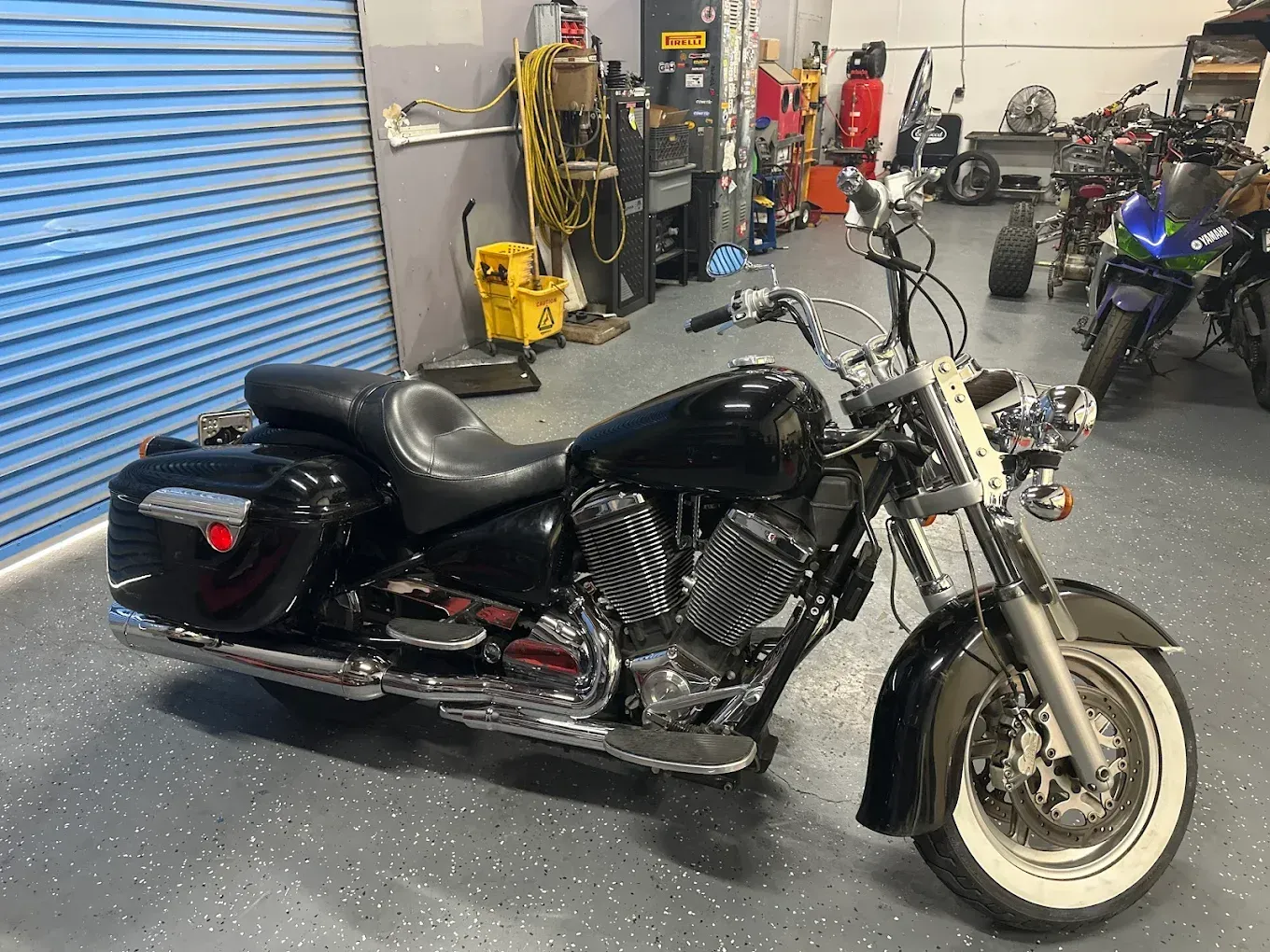 Black cruiser motorcycle with saddlebags in a garage, seen from the side.