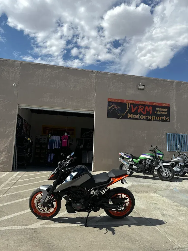 Black sport motorcycle with orange wheels parked outside a motorcycle shop under a cloudy sky