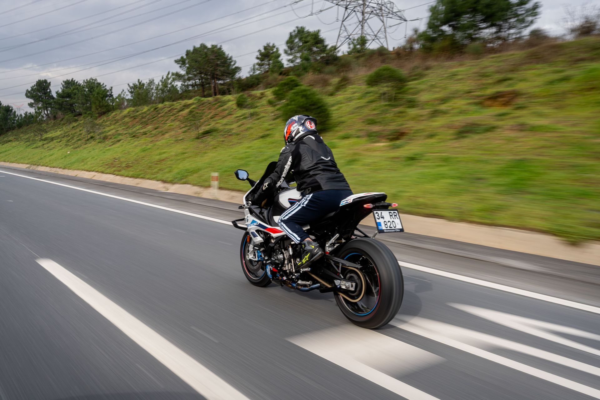 Motorcyclist riding a black sport bike on a highway with grassy roadside hills.