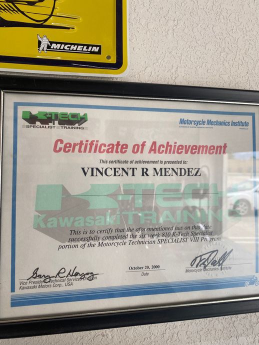 Framed Certificate of Achievement with blue border and red title on a speckled wall.