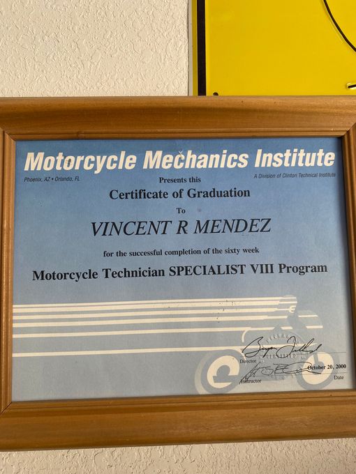 Framed Motorcycle Mechanics Institute certificate with blue text on a wall above a yellow panel