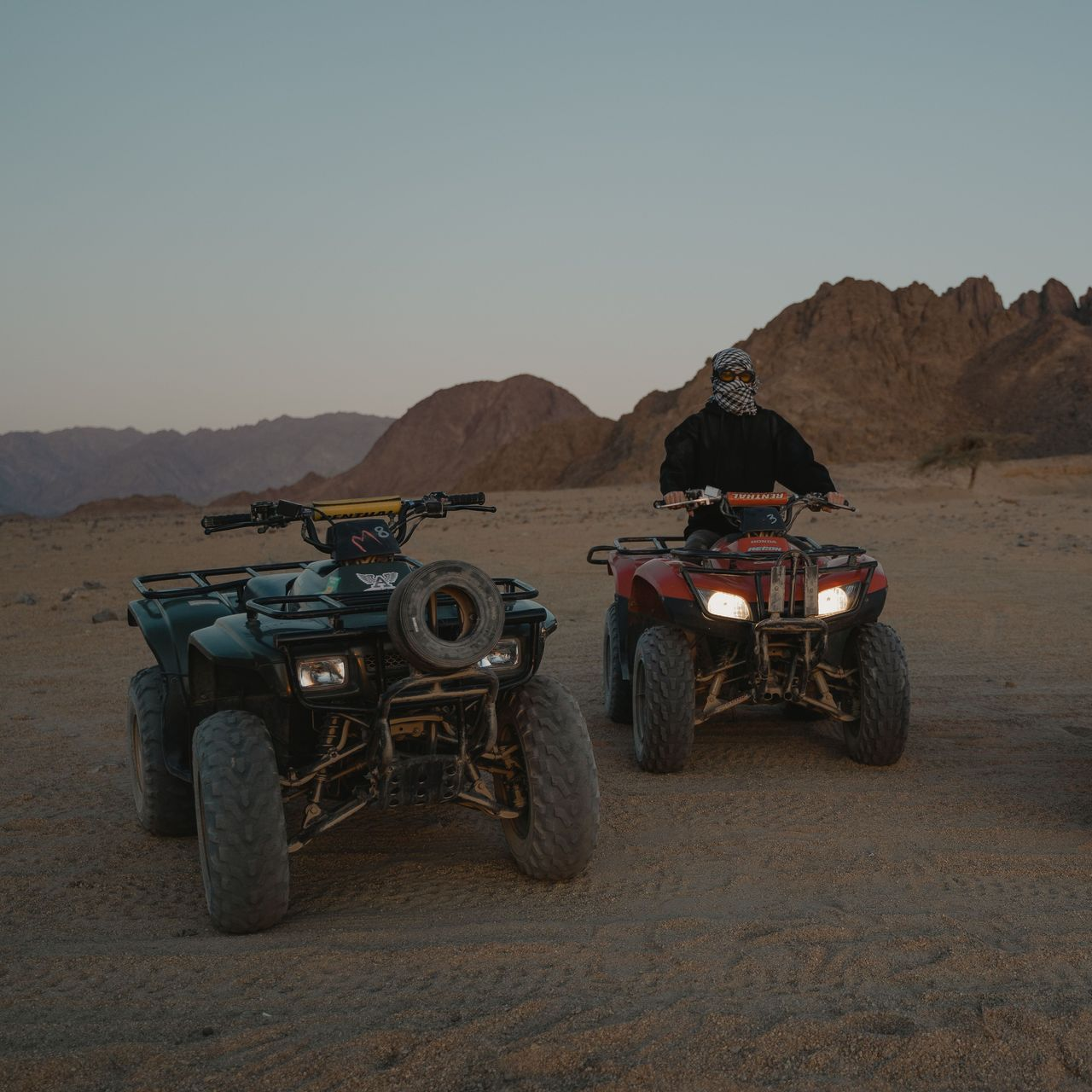 Two ATVs parked on desert dirt with mountains in the background at dusk.