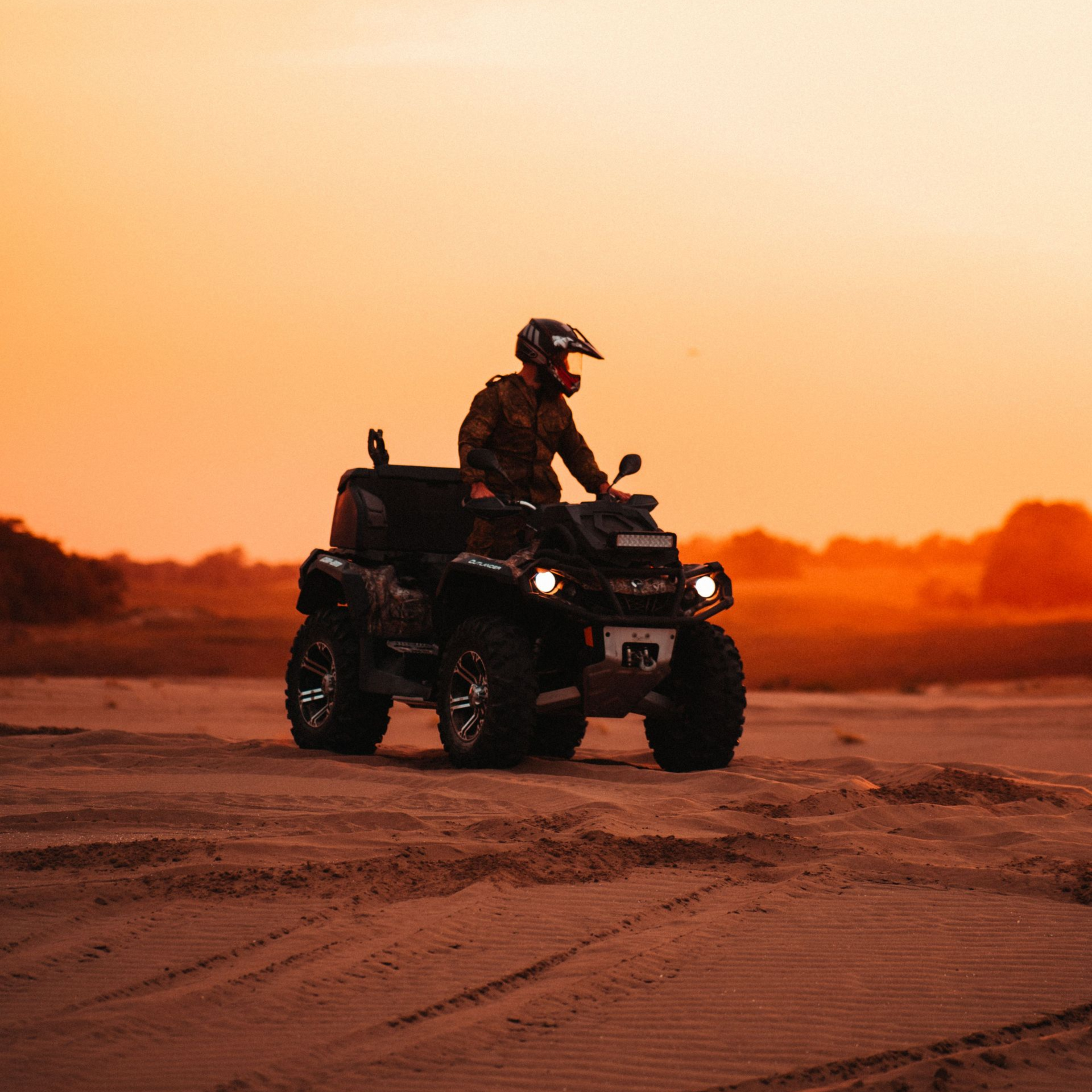 ATV rider driving across sand at sunset under an orange sky
