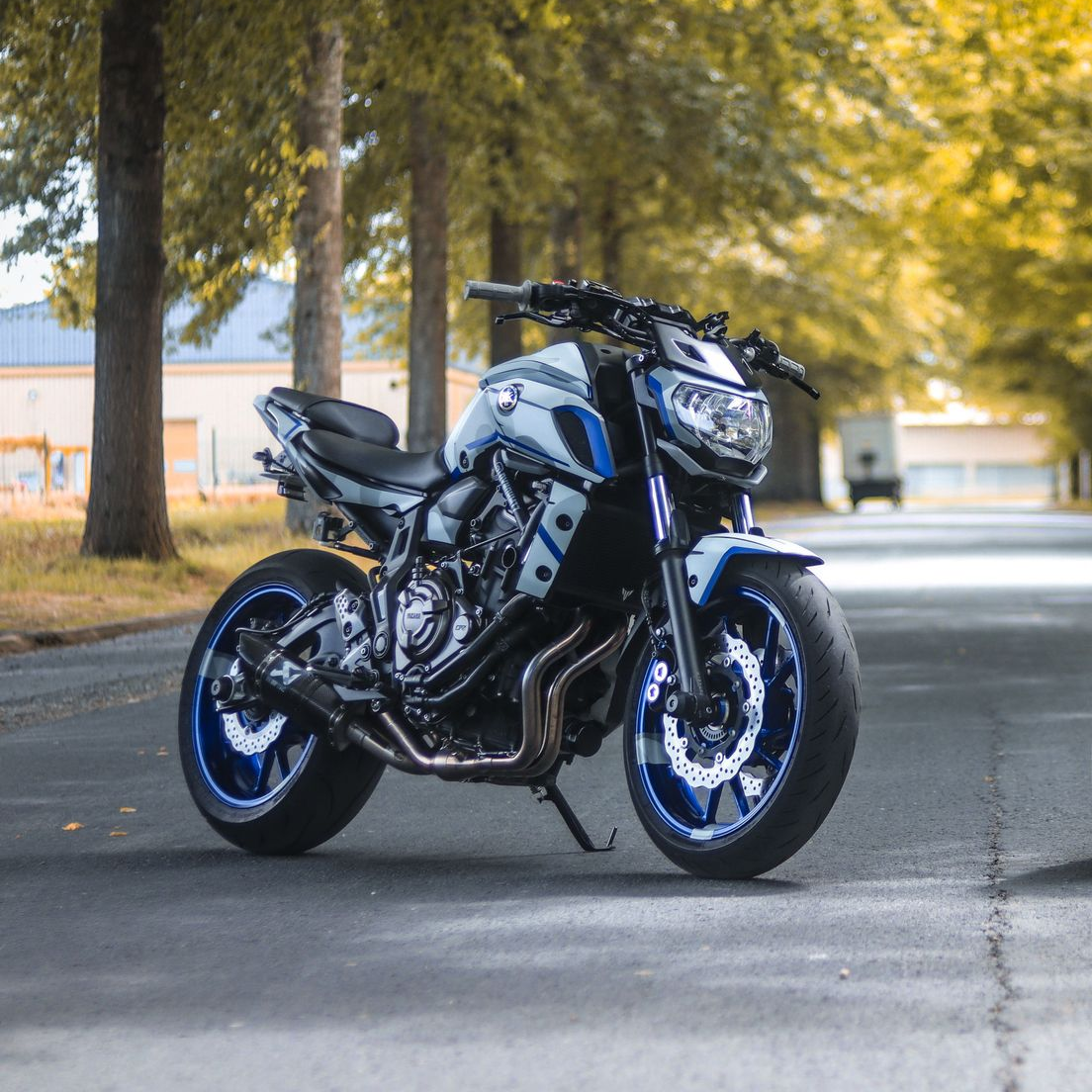 Black sport motorcycle parked on a tree-lined road with blue-rimmed wheels and a cloudy background