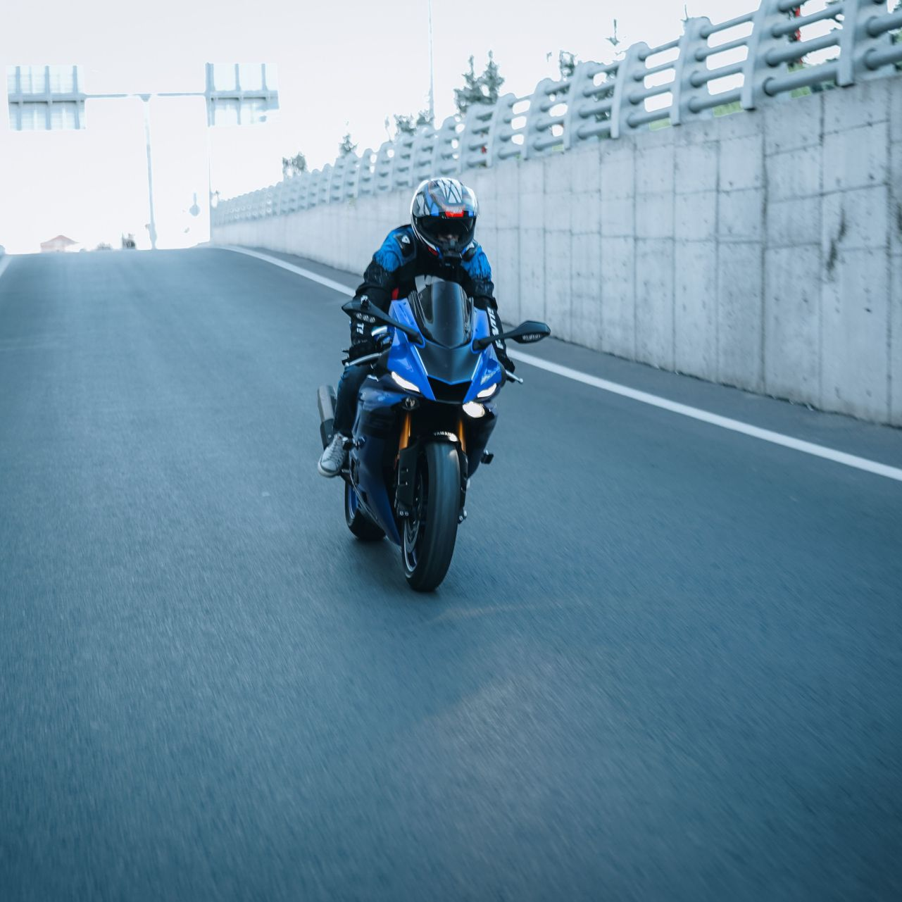 Blue sport motorcycle riding on a highway ramp beside a concrete wall