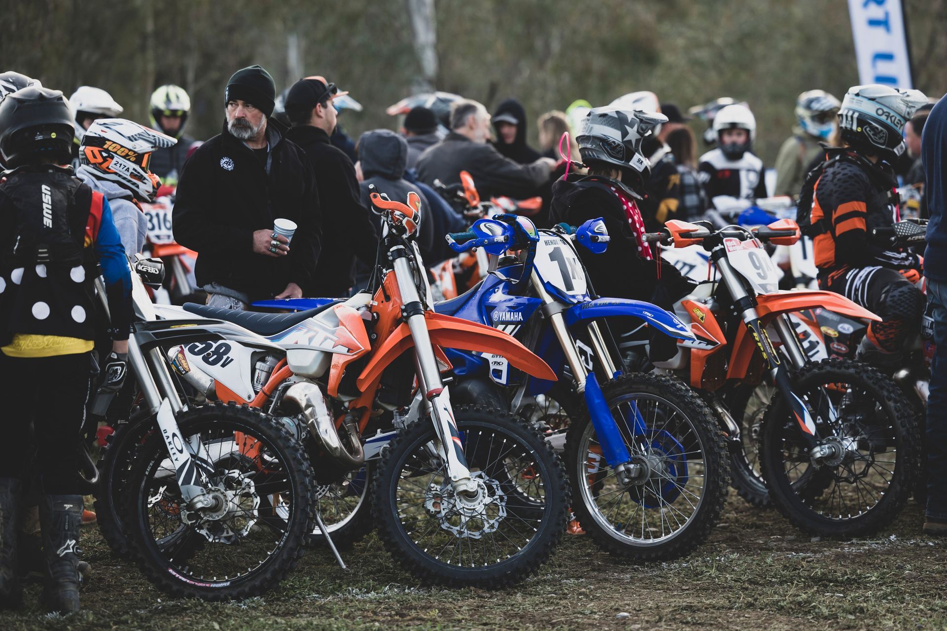 Motocross riders lined up on dirt bikes at the starting line in a crowded outdoor race.