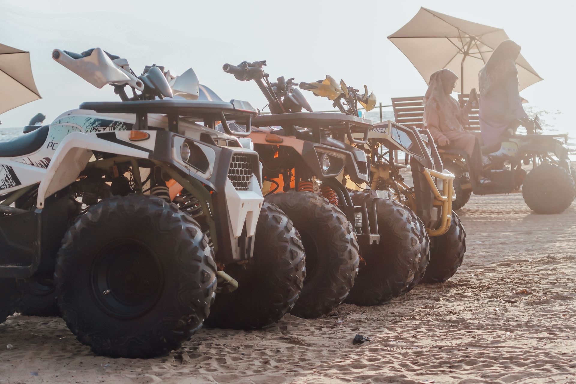 Four off-road dune buggies lined up on a sandy beach at sunset