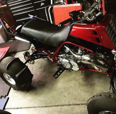 Red motorcycle with black seat in a garage, viewed from the side.
