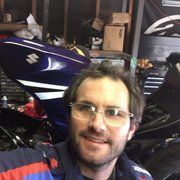 Man taking a selfie in front of a blue Suzuki motorcycle in a garage