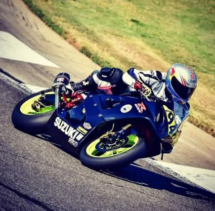 Motorcycle racer leaning hard into a turn on a blue Suzuki, track curbing visible with a blurred background