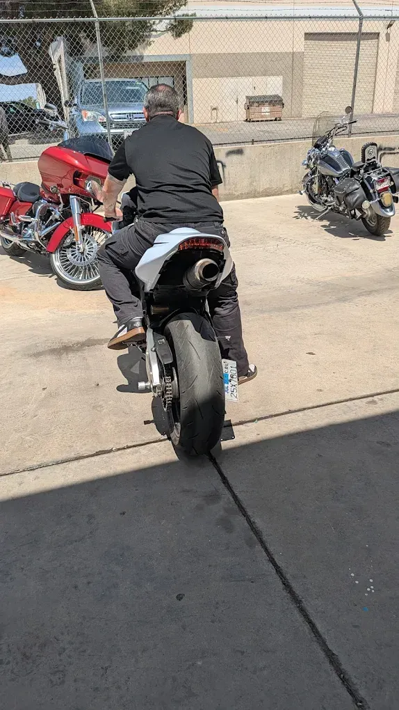 Person on a black motorcycle in a parking lot, with red and black bikes nearby.